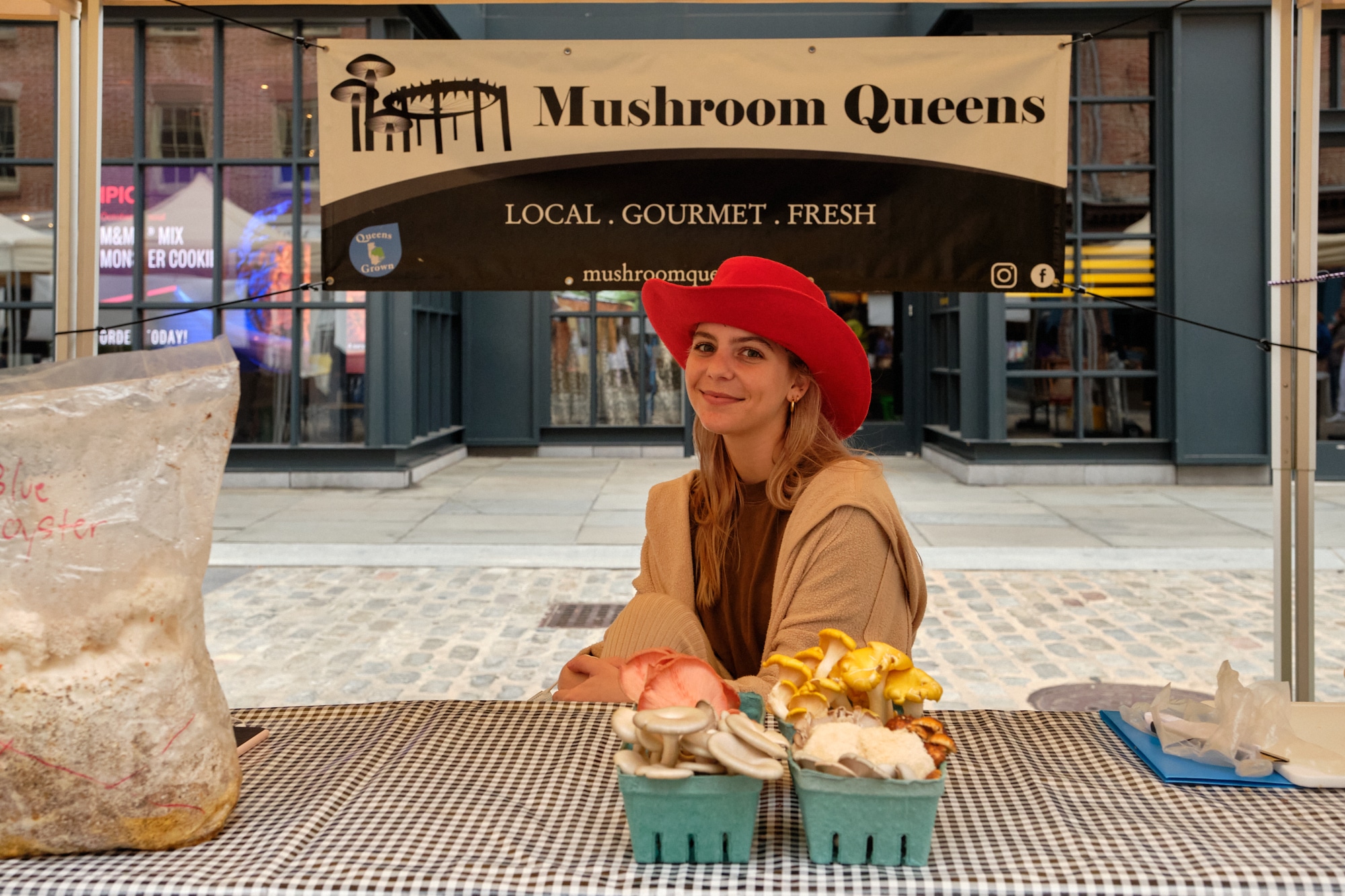 woman in a red hat at Mushroom Queens table with baskets of mushrooms