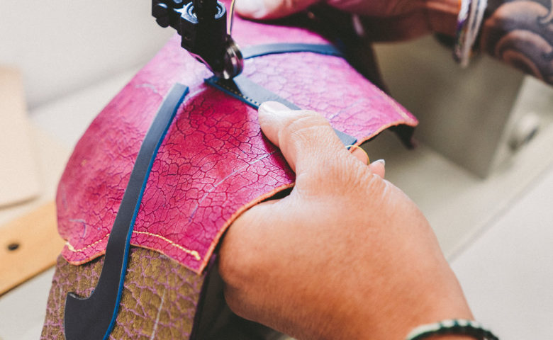person sewing a Nike swoosh onto leather