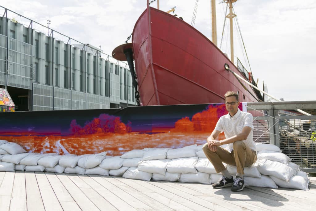 Matthew Lopez Jensen sitting in front of a banner that displays a heat map of the waterfront