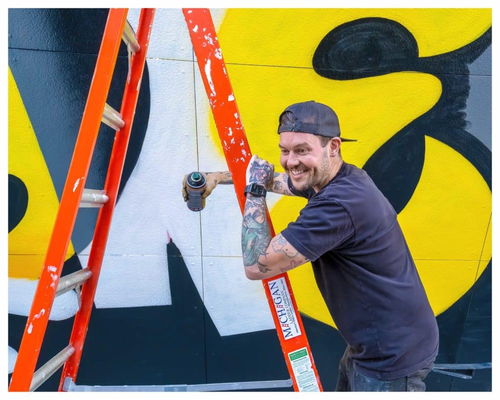 mural artist jason naylor leaning against a ladder holding can of spray paint
