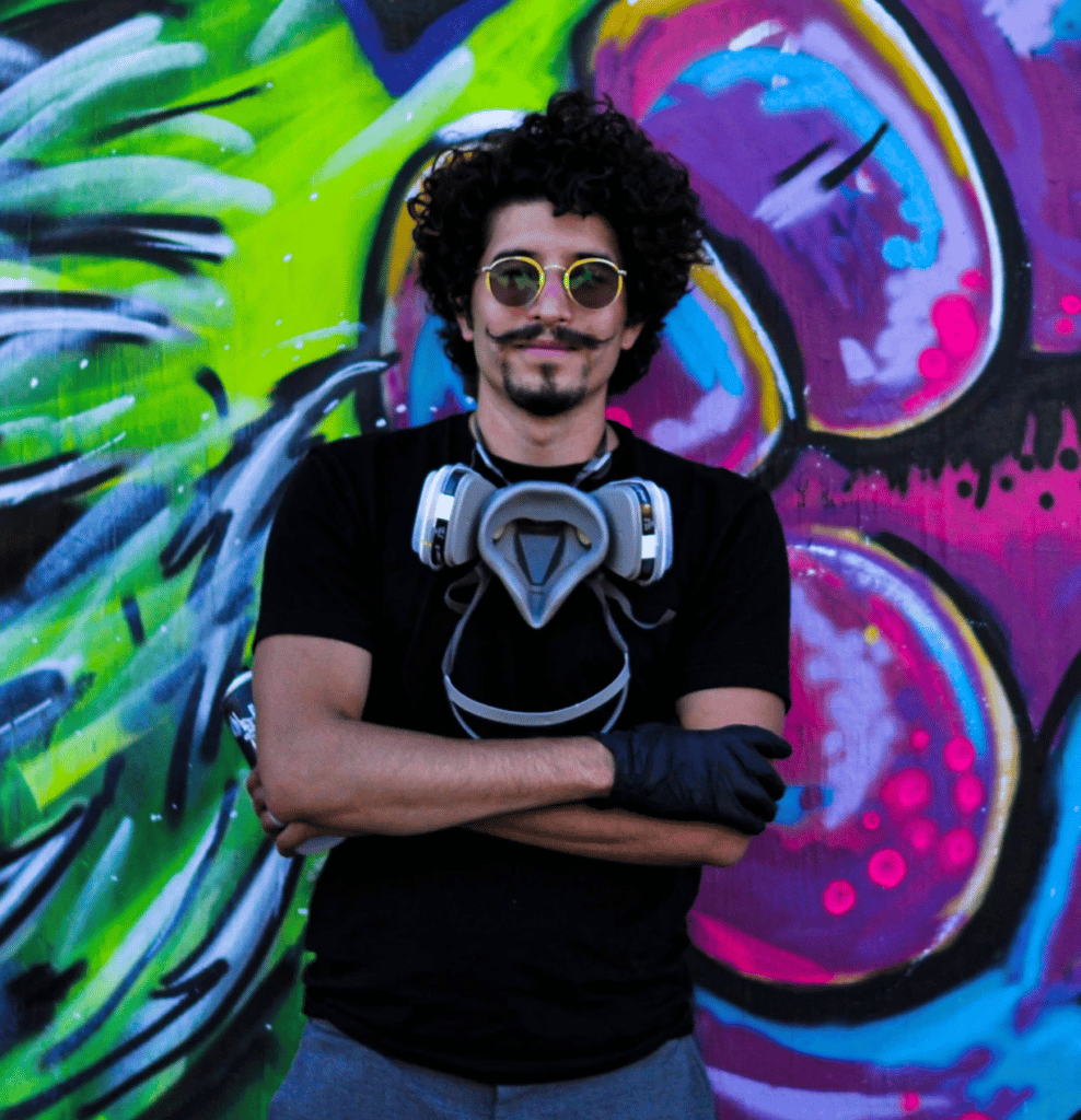 mural artist Calicho standing in front of a mural wearing sunglasses