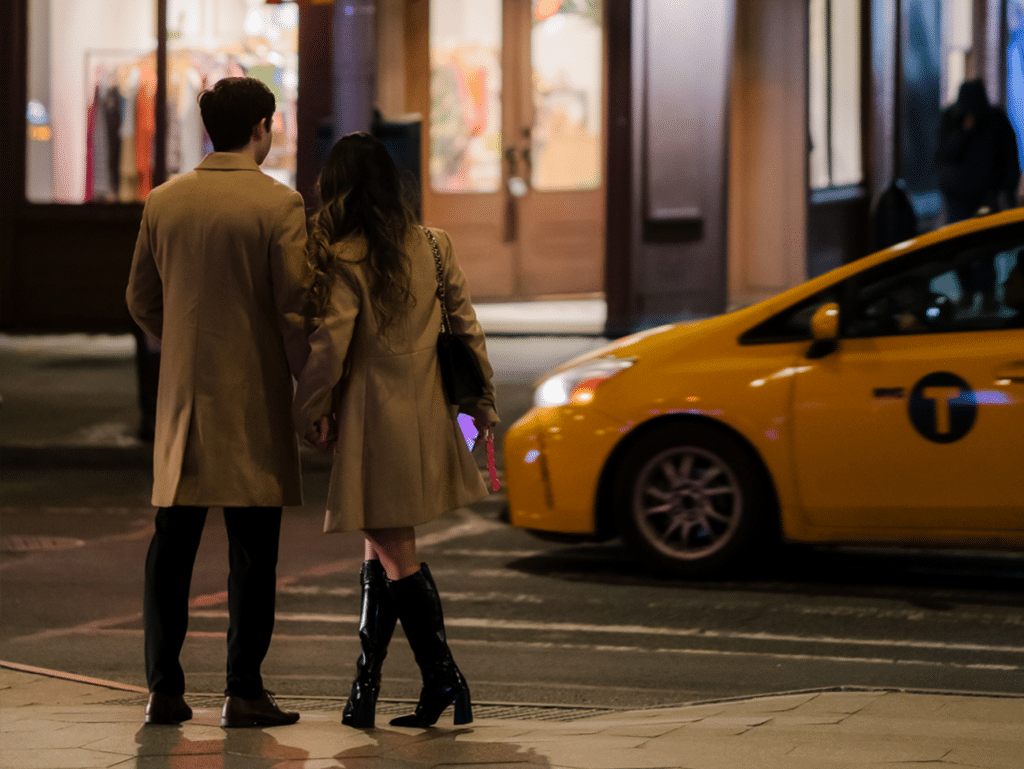 couple waiting to cross the street in front of a yellow taxi