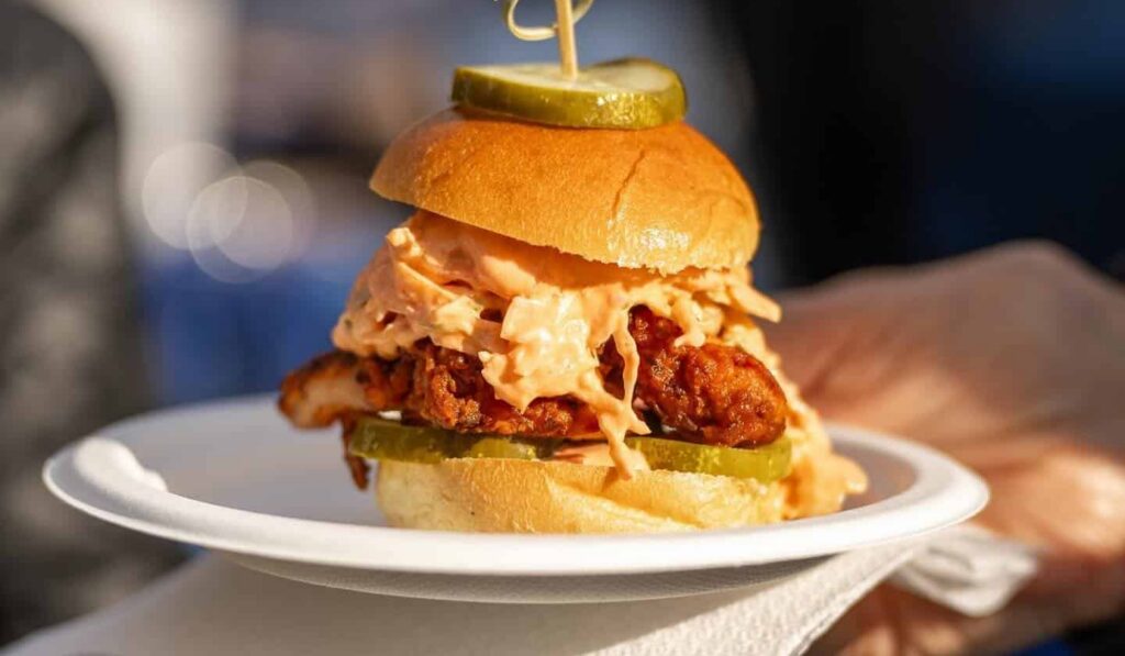 a fried chicken sandwich with slaw and pickles on a paper plate