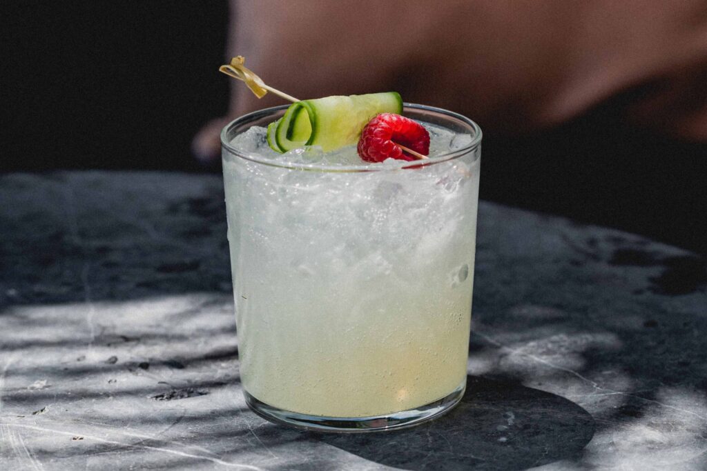 a cocktail at GITANO, garnished with a slice of cucumber and a raspberry