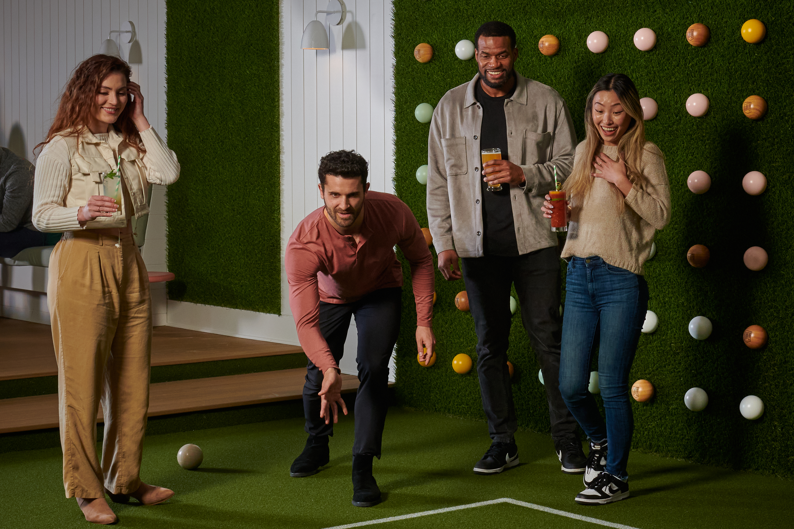 a group of young adults enjoying beverages while playing bocce indoors at lawn club