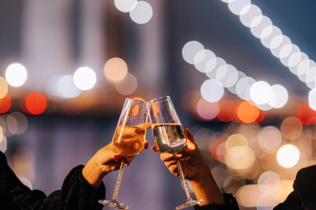 two people cheers glasses of champagne in front of the brooklyn bridge