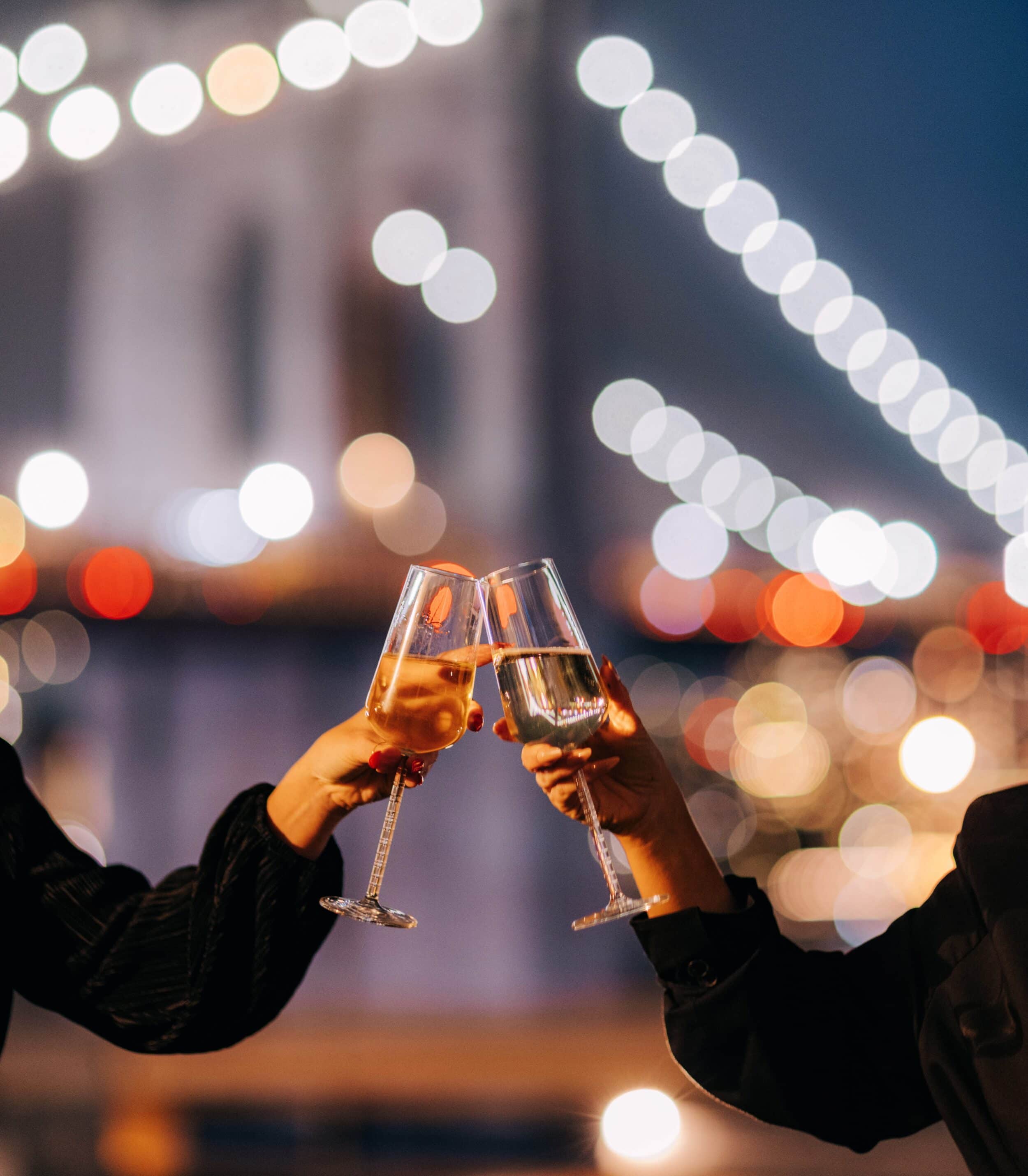 two people cheers glasses of champagne in front of the brooklyn bridge
