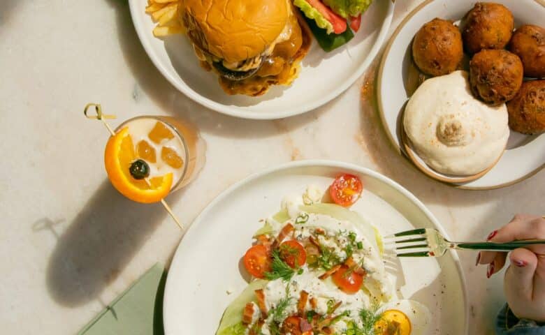 a table at sadie's with a burger, salad, and hushpuppies, with two cocktails, and light green napkins
