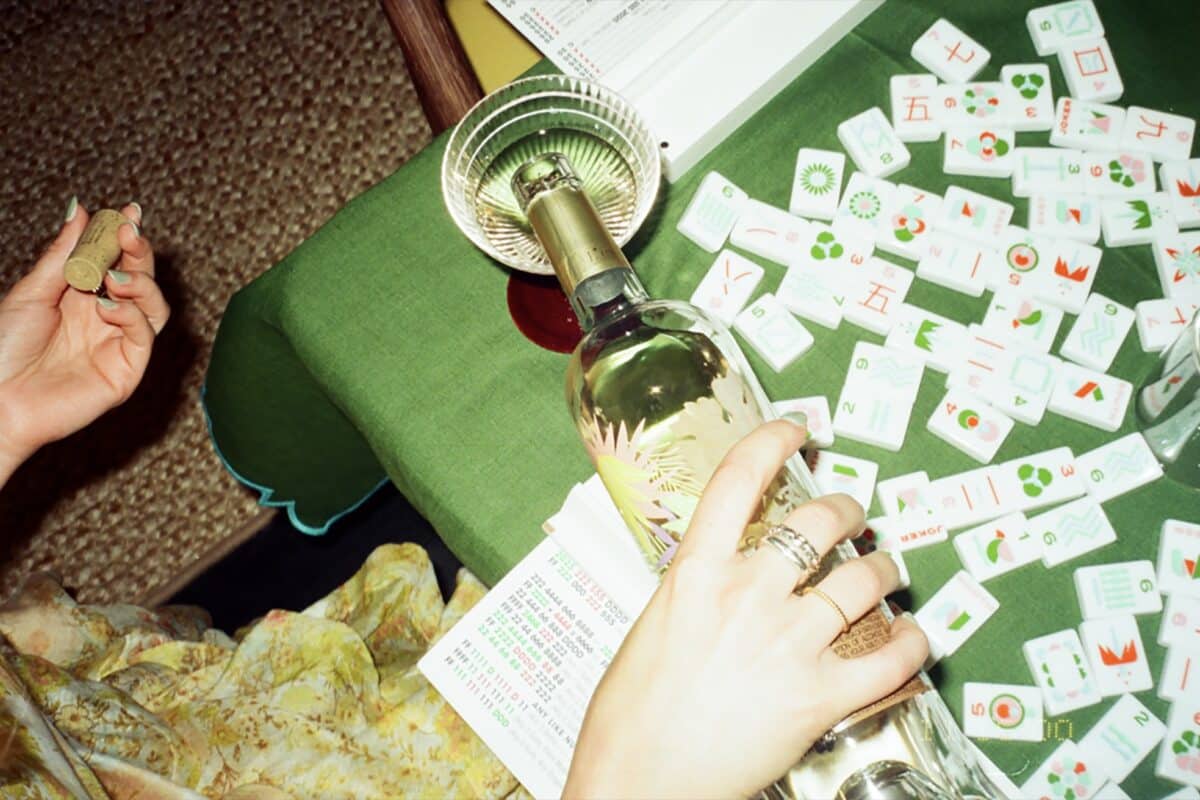 a glass of white wine being poured on a table with mahjong tiles