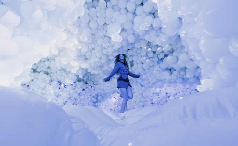 a woman bounces on an inflatable floor in a under a ceiling filled with inflated balloons, everything is light blue and dreamy