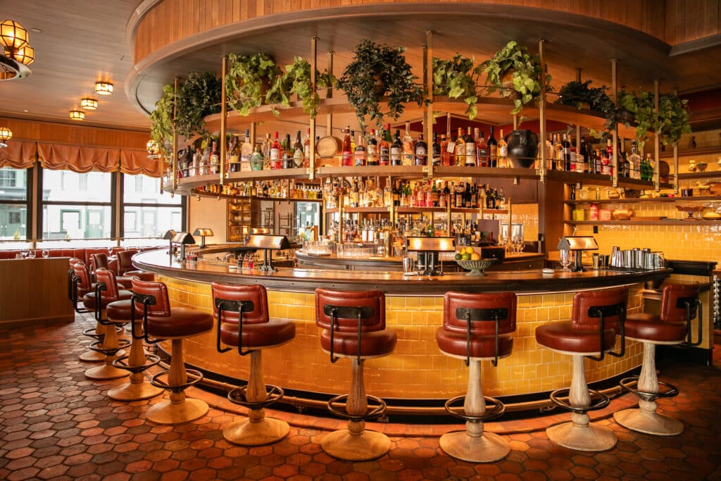 the bar at carne mare on pier 17 - warmly lit round wooden bar with brown leather stools and pops of greenery