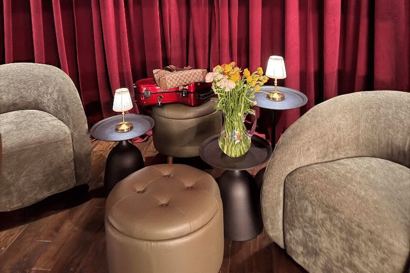 the interior lounge area of cork wine bar at the seaport - two grey armchairs in front of a dark red curtain. a small ottoman and side table sit between them
